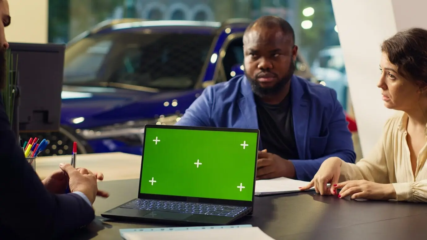 Продавец автосалона просматривает список встреч в электронной таблице на ноутбуке с хромакеем.